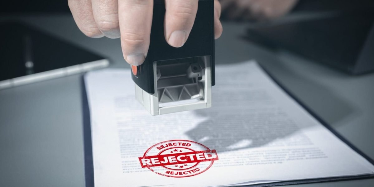 Person stamping a document with a red 'REJECTED' stamp visible on the page underneath.